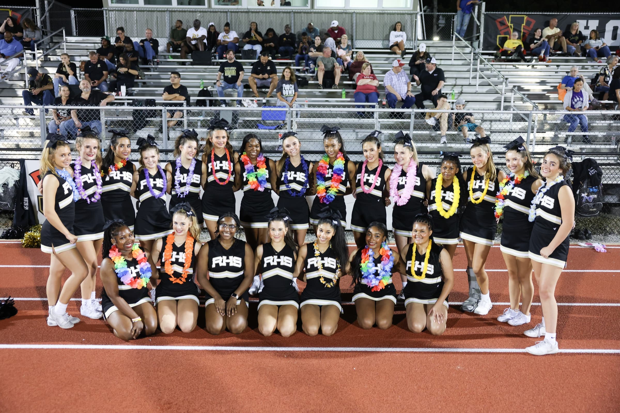 A high school cheer team poses together beside the track at a football stadium.
