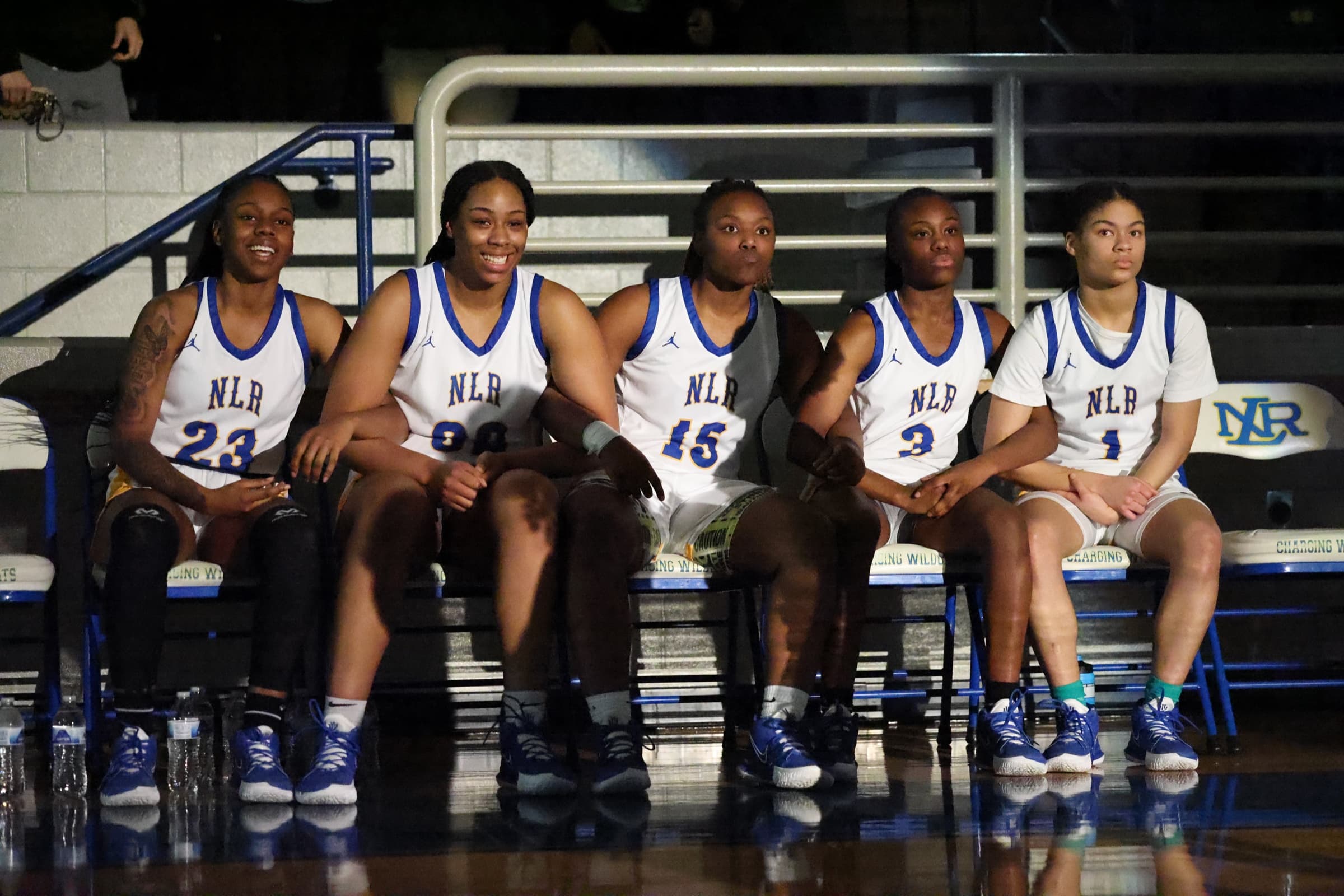 Girls basketball players sit together on the team bench during a game.
